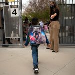 A kindergartener leaves Maurice Sendak Elementary School. He is wearing a large dinosaur themed backpack.