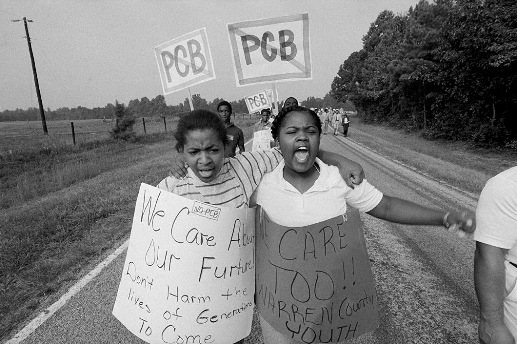 Two young girls wear protest signs that read "We Care About Our Future! Don't harm the lives of generations to come." and "We care too!! Warren County Youth"