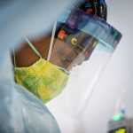 A nurse adjusts an electrode on a COVID-19 patient on a ventilator.