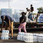 People grab packs of water bottles from a truck bed.