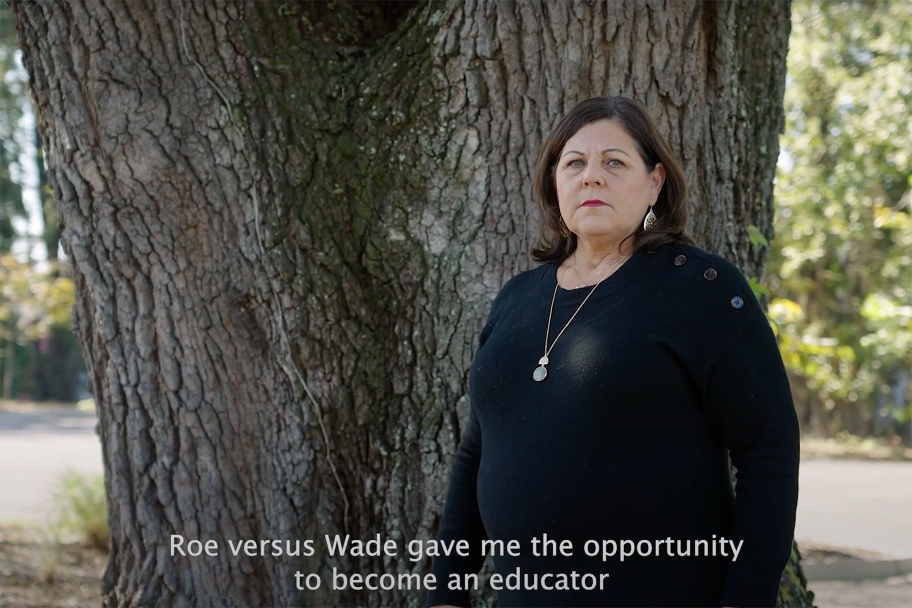 screenshot from South Carolina governor candidate Joe Cunningham’s newest ad in which a woman named Fran shares her abortion story. She is seen here standing near a tree and looking at the camera. The subtitles read "Roe versus Wade gave me the opportunity to become an educator."
