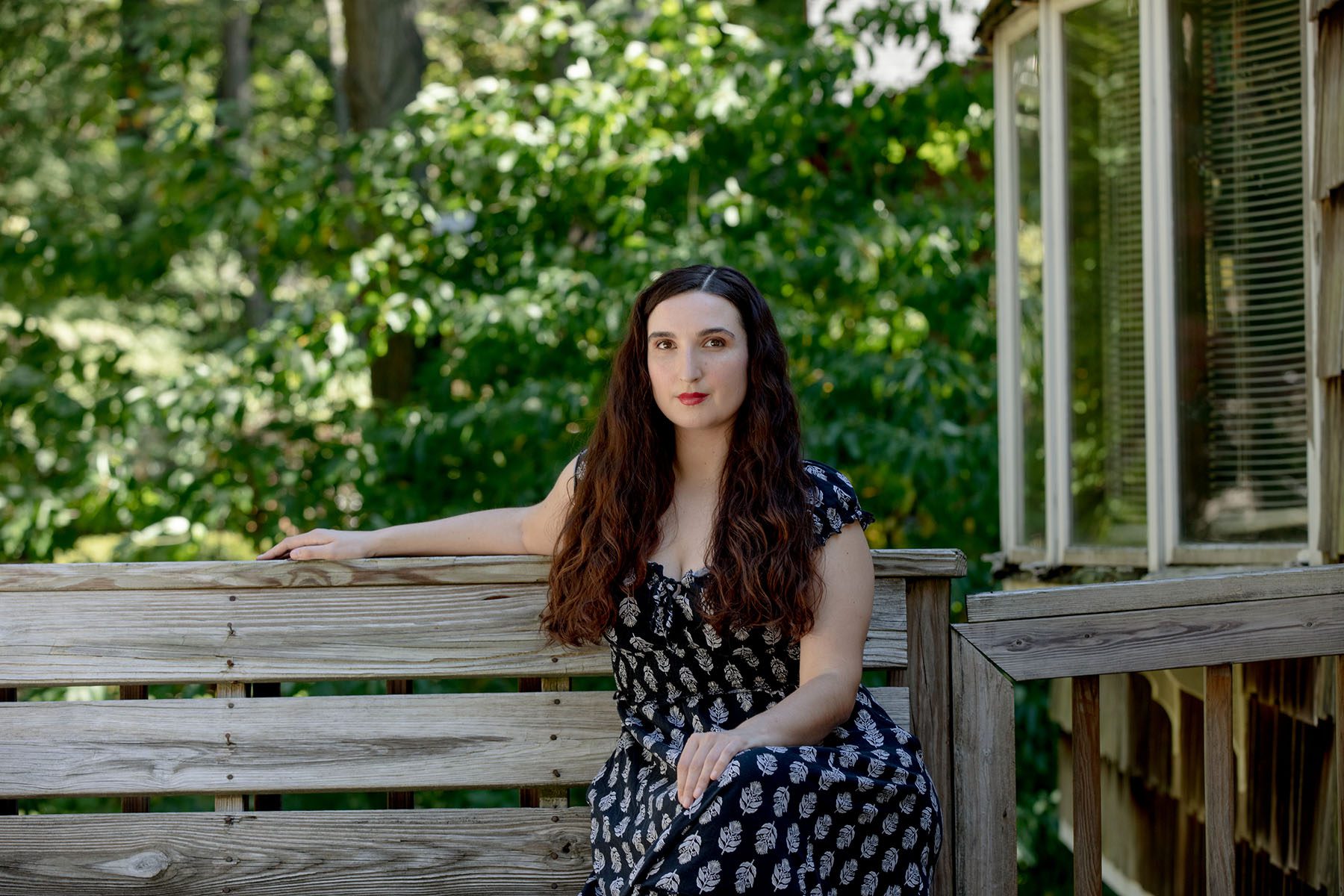Sarah Anne Mass poses for a portrait while sitting on an old wooden bench on a deck.