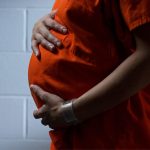 person in orange jumpsuit holds pregnant belly