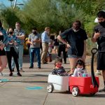 People wait in line outside a polling place including a family in the foreground with two little girls in a toy wagon.