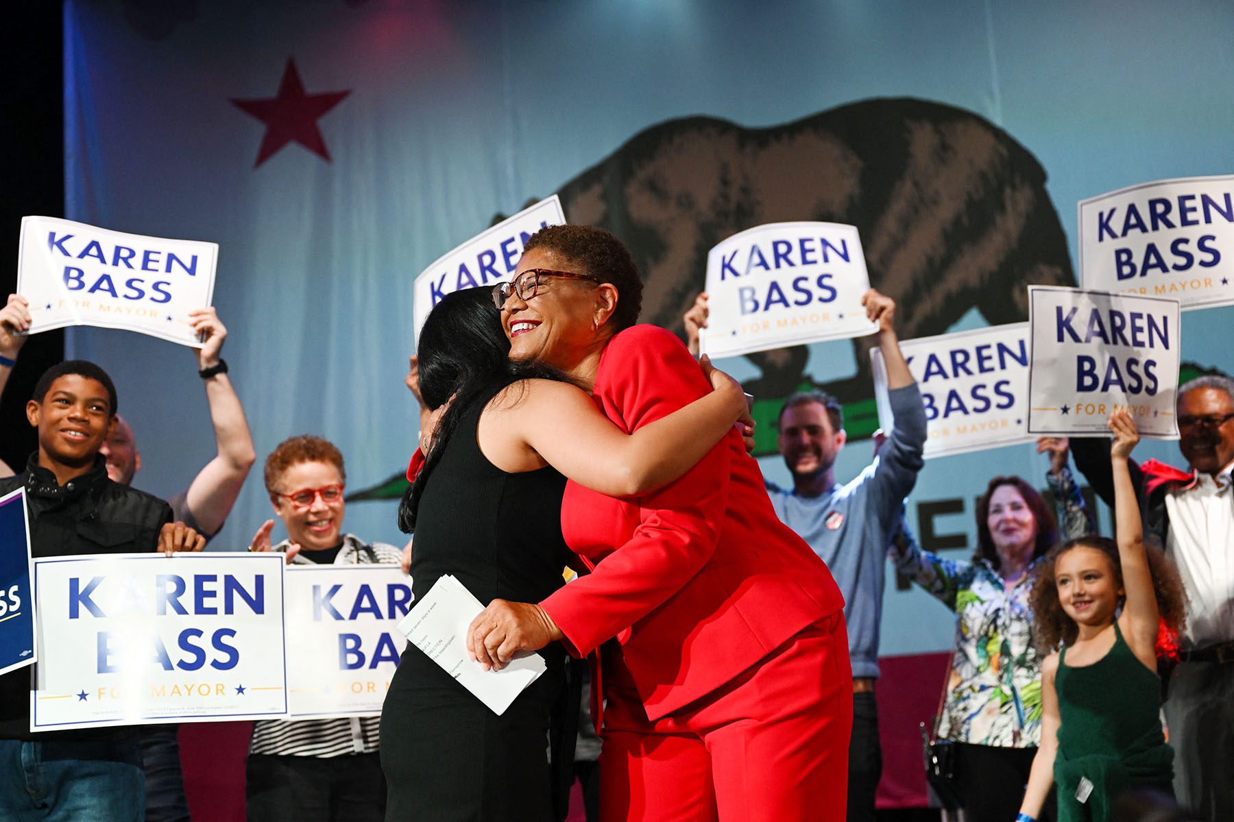 Karen Bass hugs her daughter as supporters holding "Karen Bass for Mayor" smile and cheer.