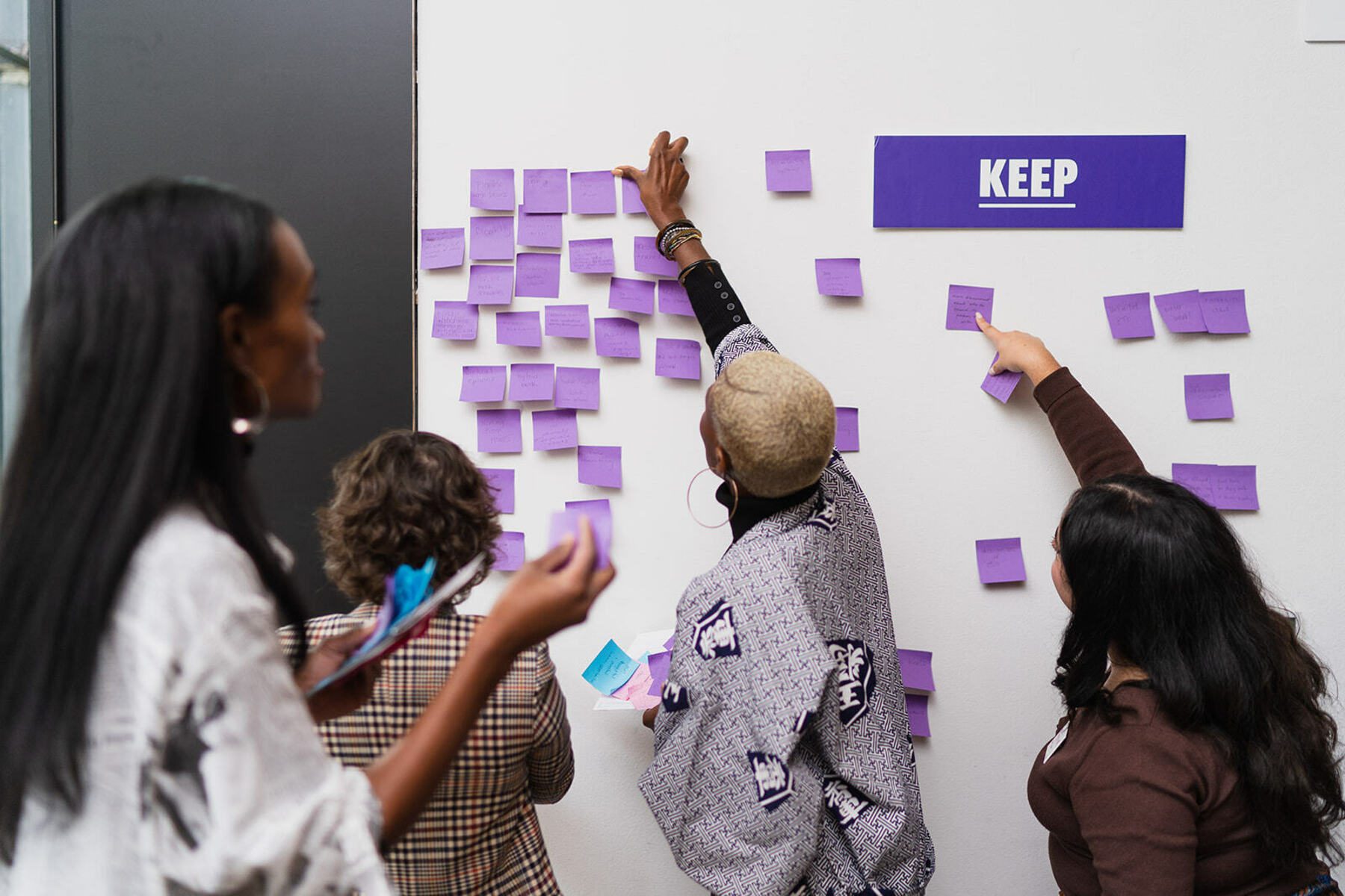A person pastes a purple sticky note on a white wall.