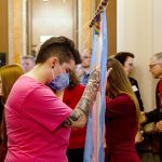 Becky Smith holds a transgender flag banner as Iowa Governor Kim Reynolds signs a bill which bans transgender girls from participating in girls sports at the Iowa State Capitol.