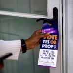 A volunteer places a door tag in support of Proposal 3 on a door. The tag read 