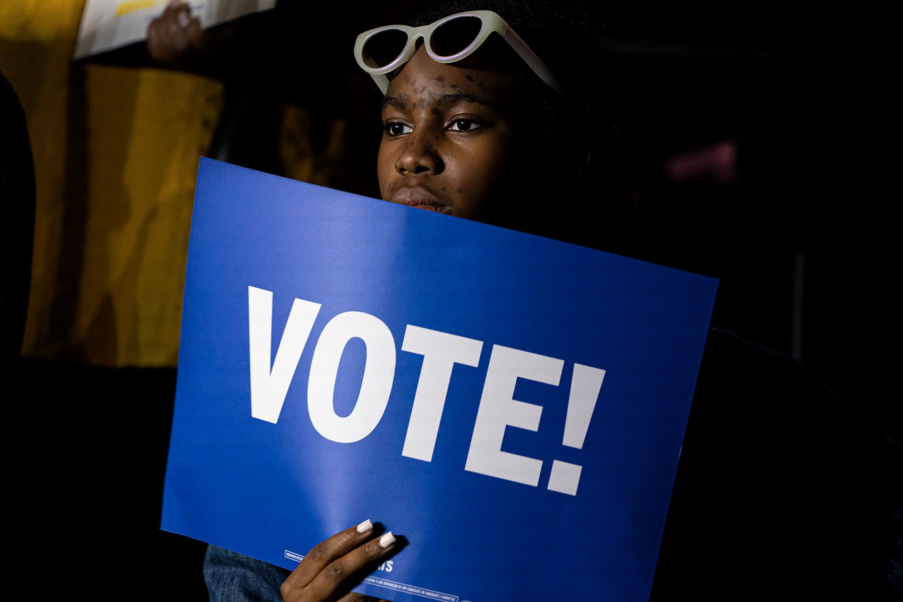 A supporter holds a blue sign that reads "vote!" at a campaign rally for Wes Moore.