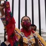 A demonstrator in indigenous garb holds up her fist in front of the White House.