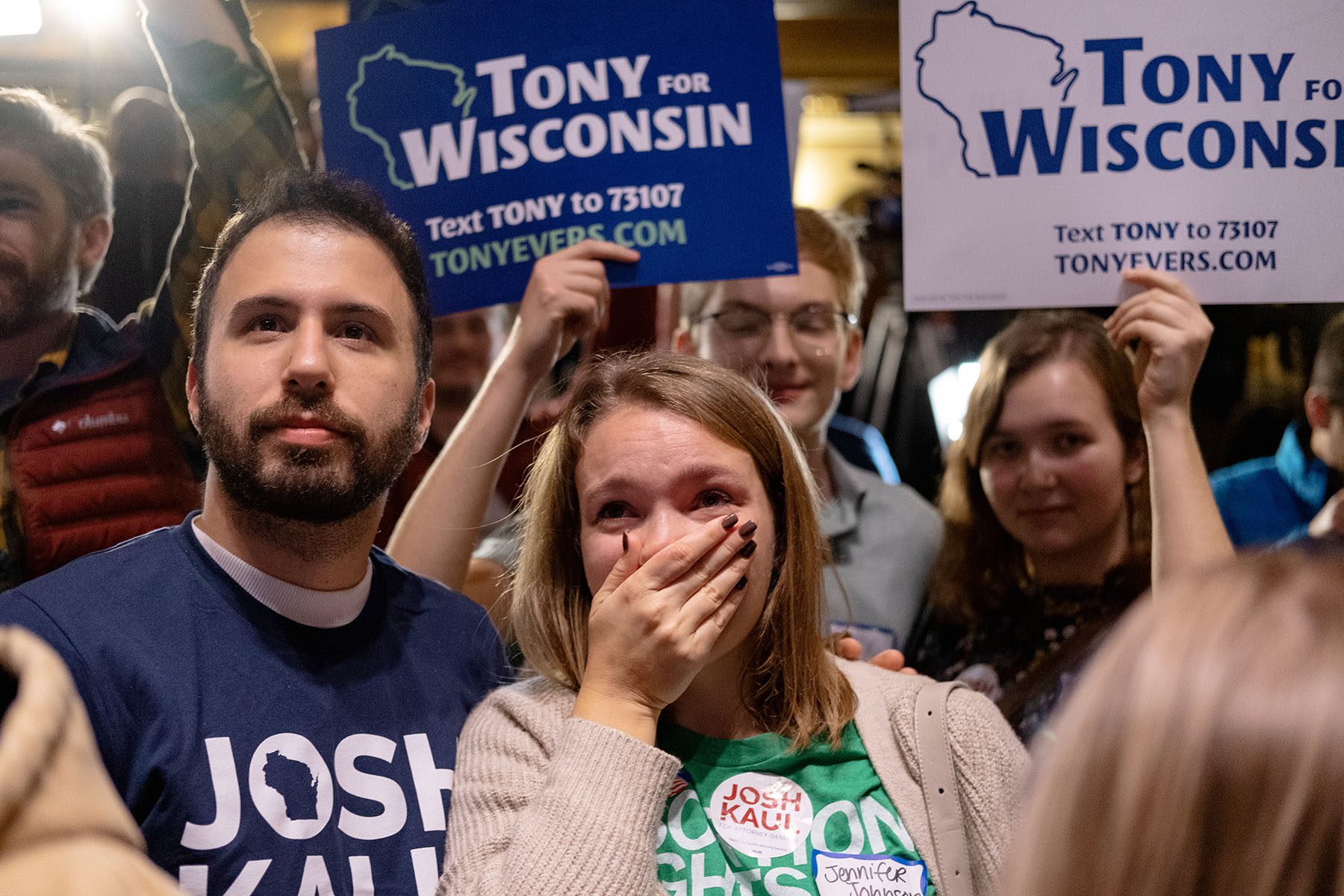 A woman looks emotional as she covers her face in disbelief as others smile and hold "Tony for Wisconsin" signs around her.