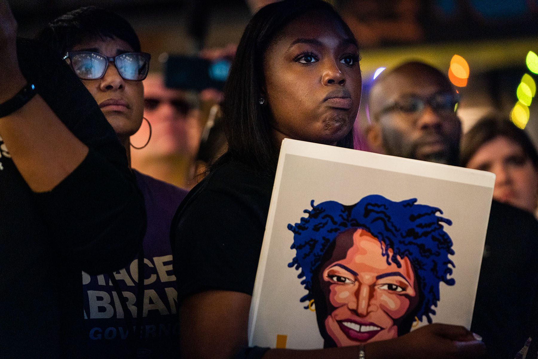 A woman holds a portrait of Stacey Abrams as she listens to Abrams speak.