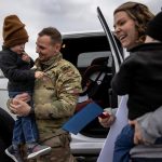 A U.S. Army Staff Sargent holds his son in his arms and smiles as his spouse holds their other child.