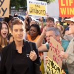 Still from an episode of TV show Grey's Anatomy in which a character is seen walking through a crowd of anti-abortion protesters.