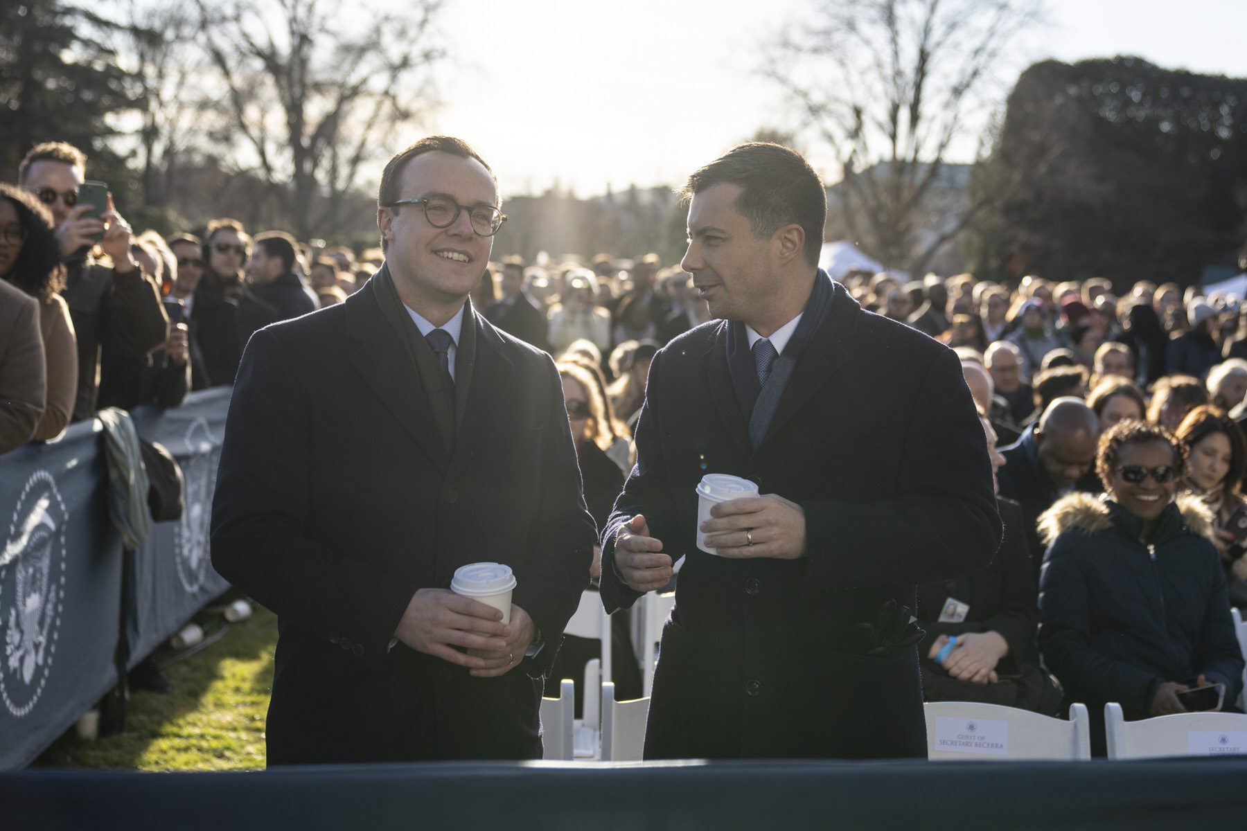 Chasten and Pete Buttigieg stand outside with crowds in the background