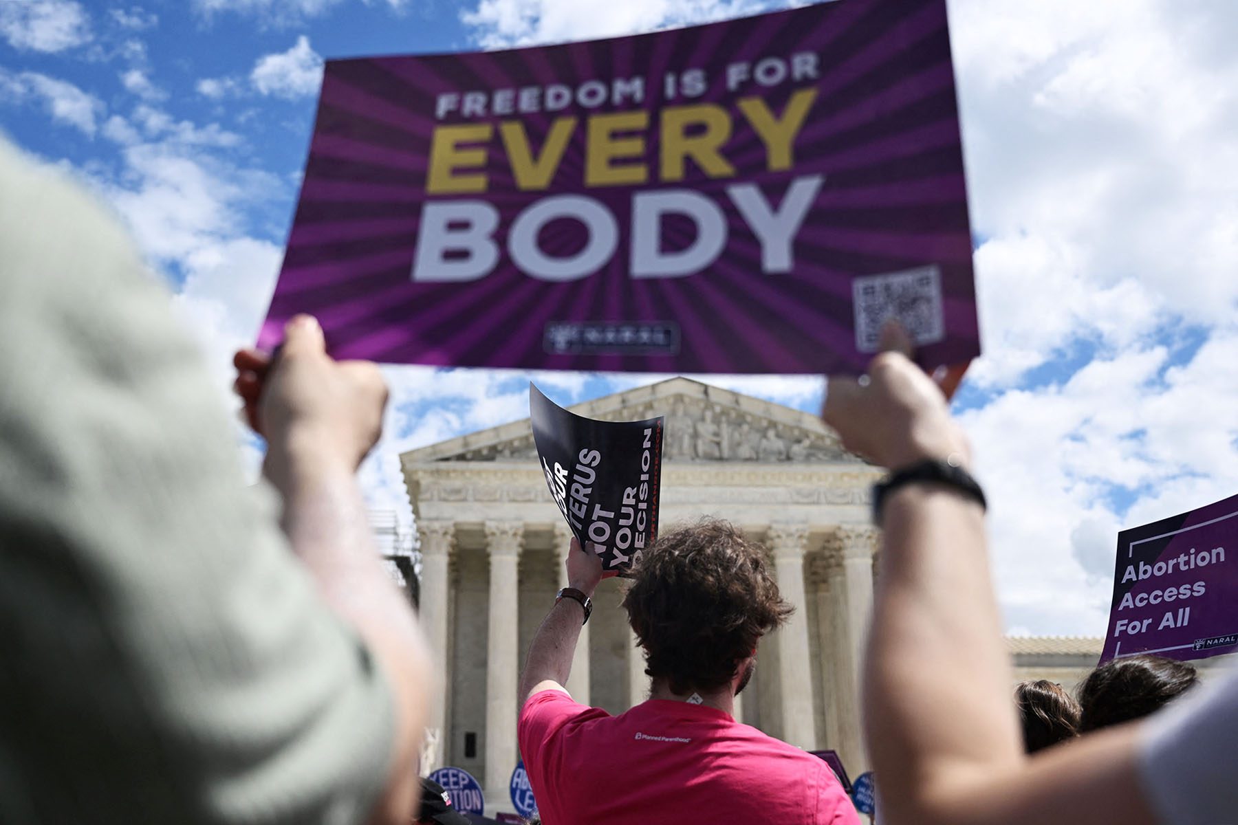 Demonstrators rally in support of abortion rights in front of the Supreme Court. A sign that reads "Freedom is for Everybody" can be seen in the foreground, and one that reads "abortion access for all" on the right side of the frame.