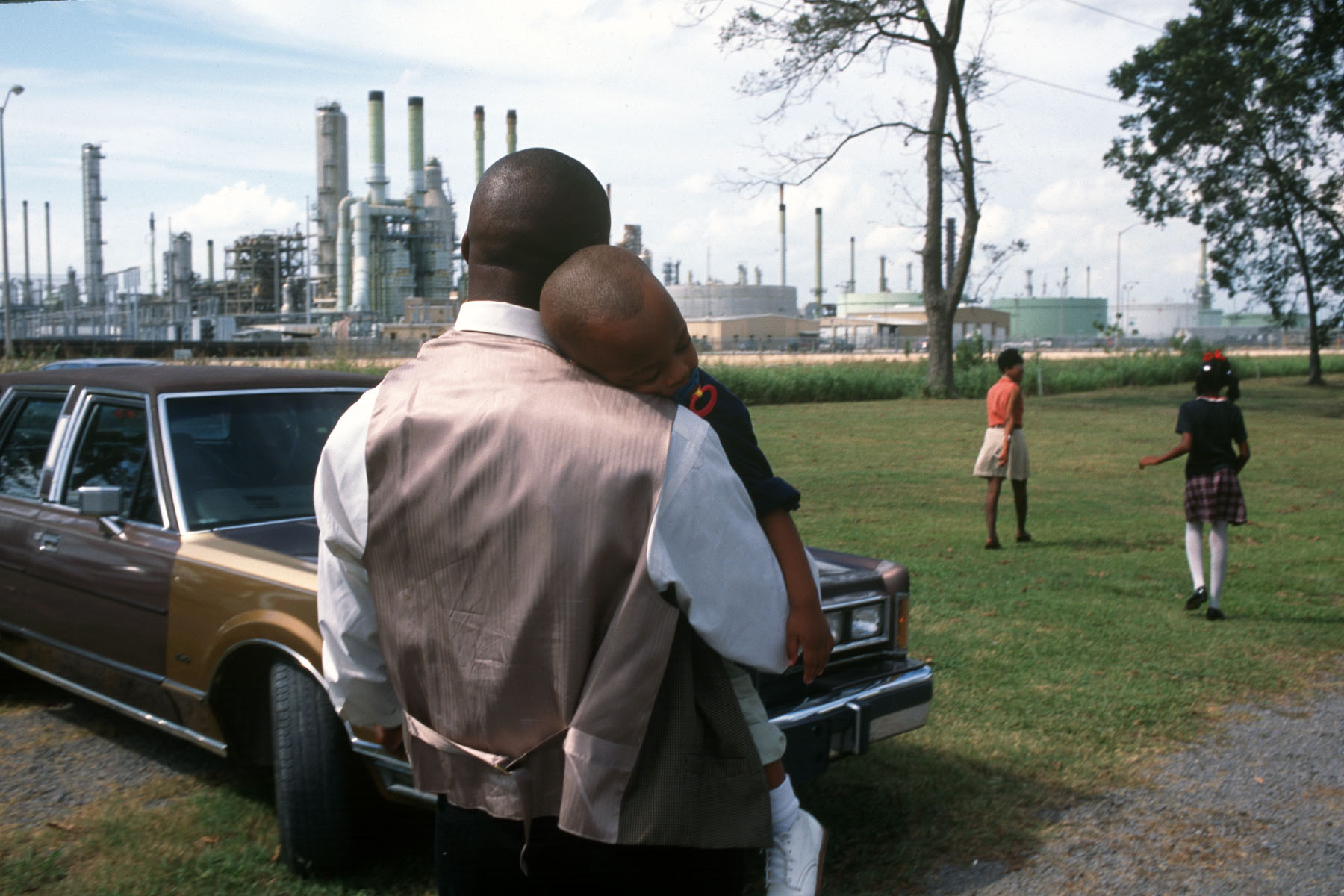 A dad holds his sleeping son as a family leaves Sunday church services surrounded by chemical plants in October of 1998 in Lions, Louisiana.