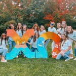 A group of people cluster around two giant Greek letters that spell out Chi Omega.