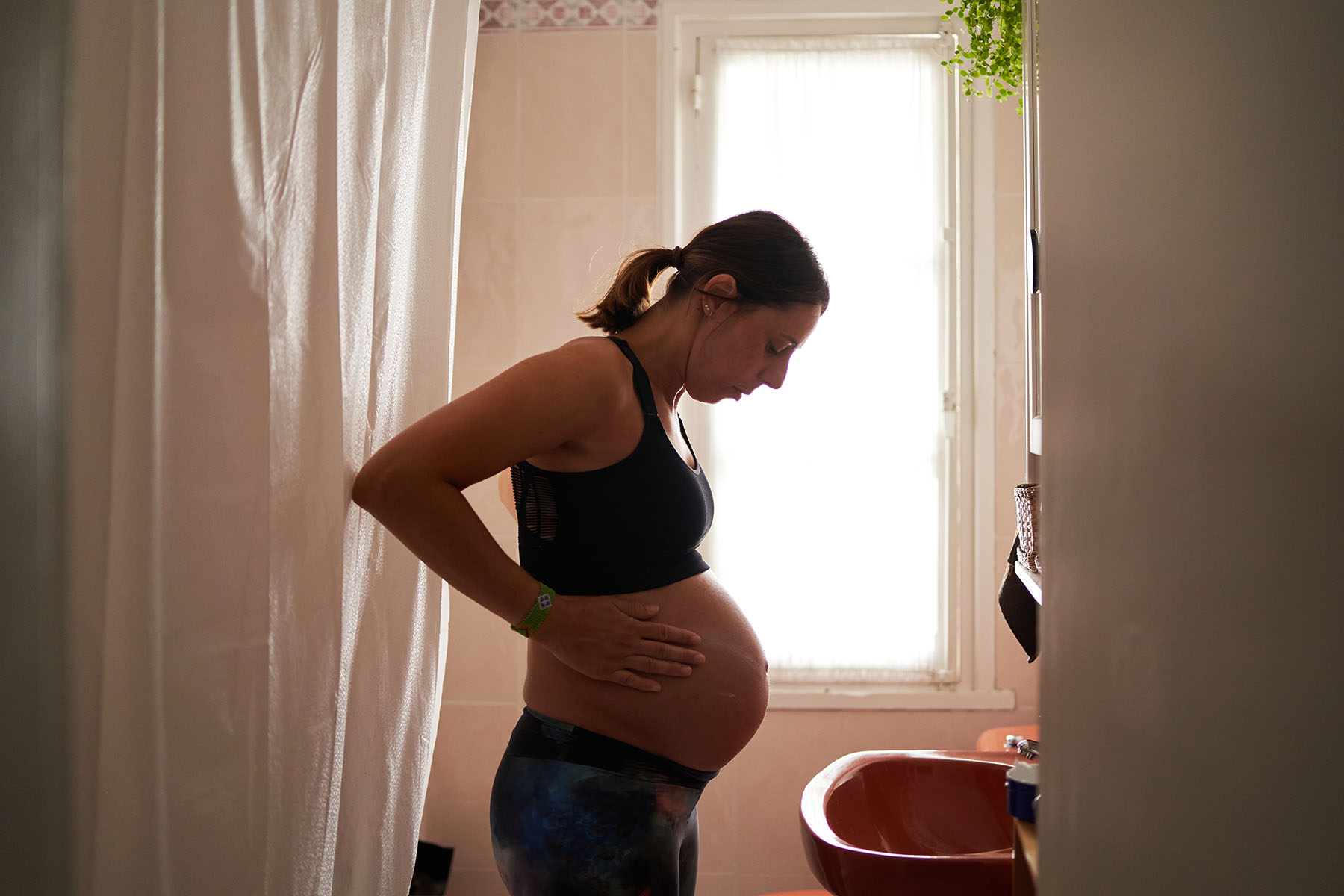 Side view of pregnant woman in her bathroom at home moisturizing her belly in a bathroom.