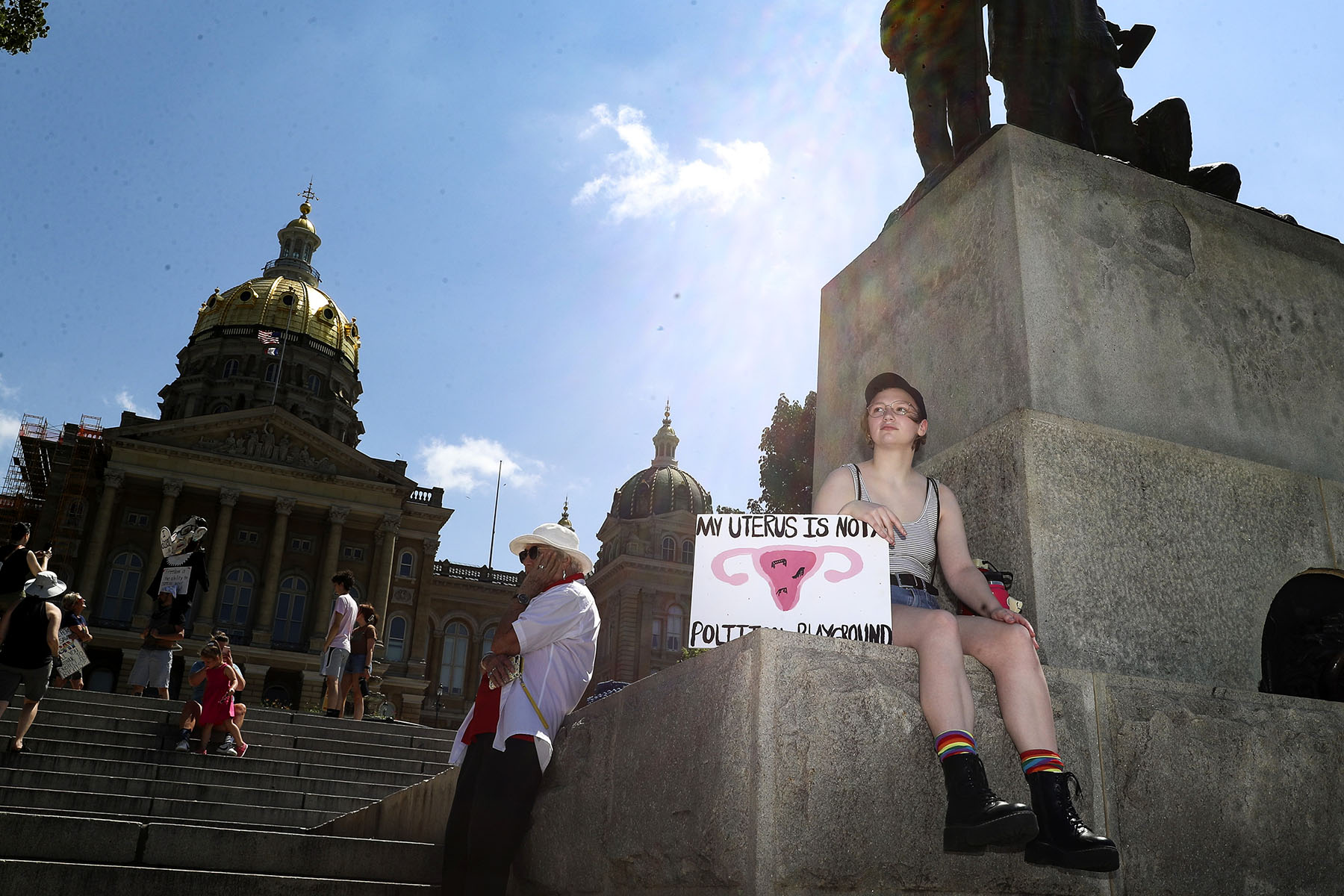 An abortion rights protester waits for the start of a rally for reproductive freedom on at the Iowa State Capitol Building. They hold a sign that reads "My uterus is not your political playground."