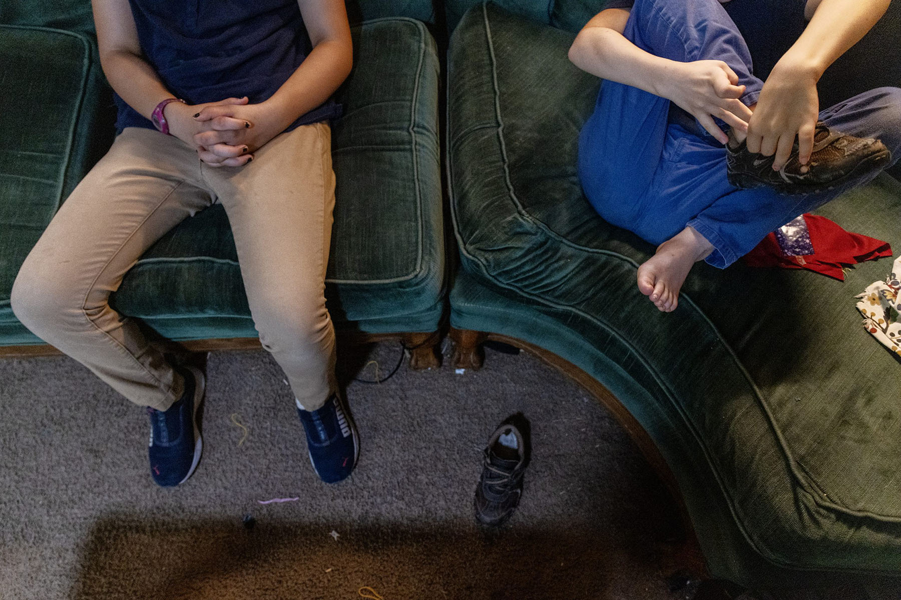 Two Bauman kids sit on a sofa putting their shoes on.