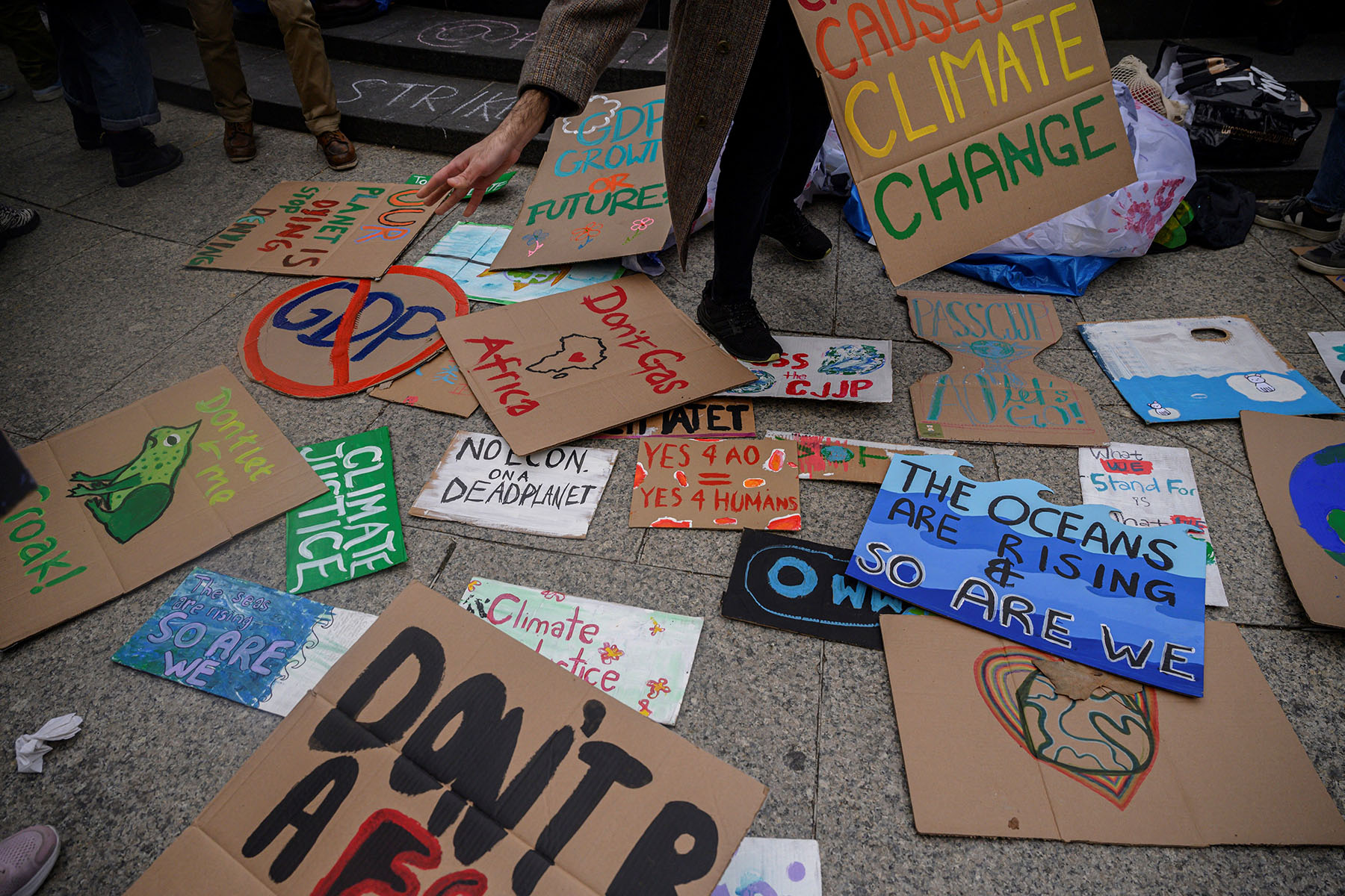 An activist picks up a placard during a Global Climate Strike. Posters are all over the floor and read "The oceans are rising and so are we," "climate justice," "no Econ on a dead planet"