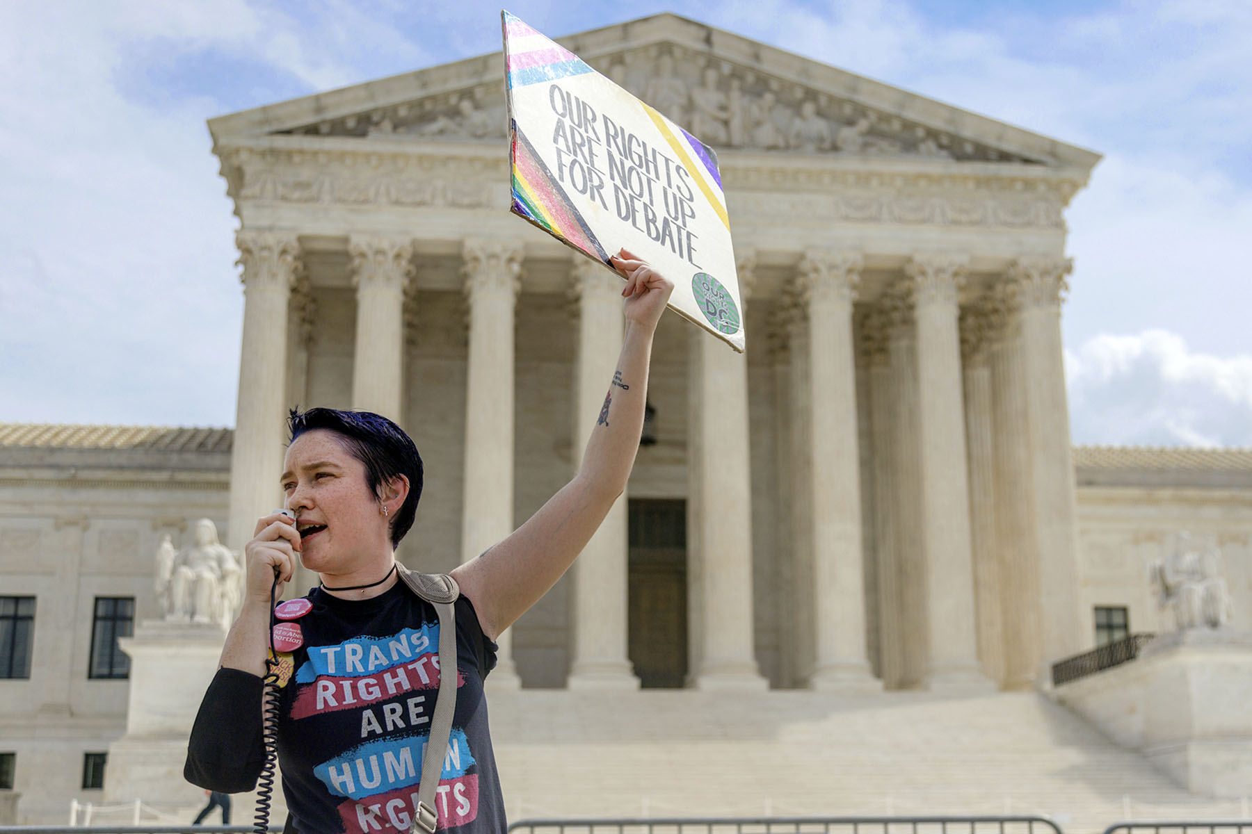 A demonstrator outside the Supreme Court in Washington, D.C. wears a "Trans Rights are human rights" shirt and speaks into a megaphone.