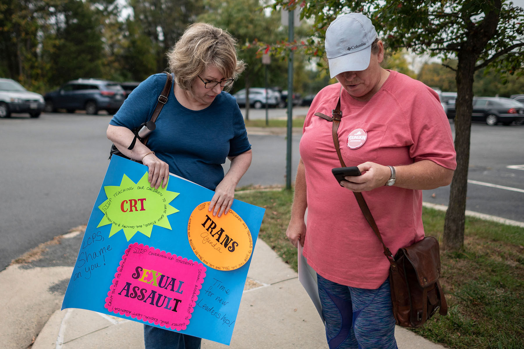 Protesters stand outside a Loudoun County Public Schools board meeting in Ashburn, Virginia in October 2021. One hold a signs that reads "Trans Agenda, CRT, Sexual Assault, Time for new leadership!"