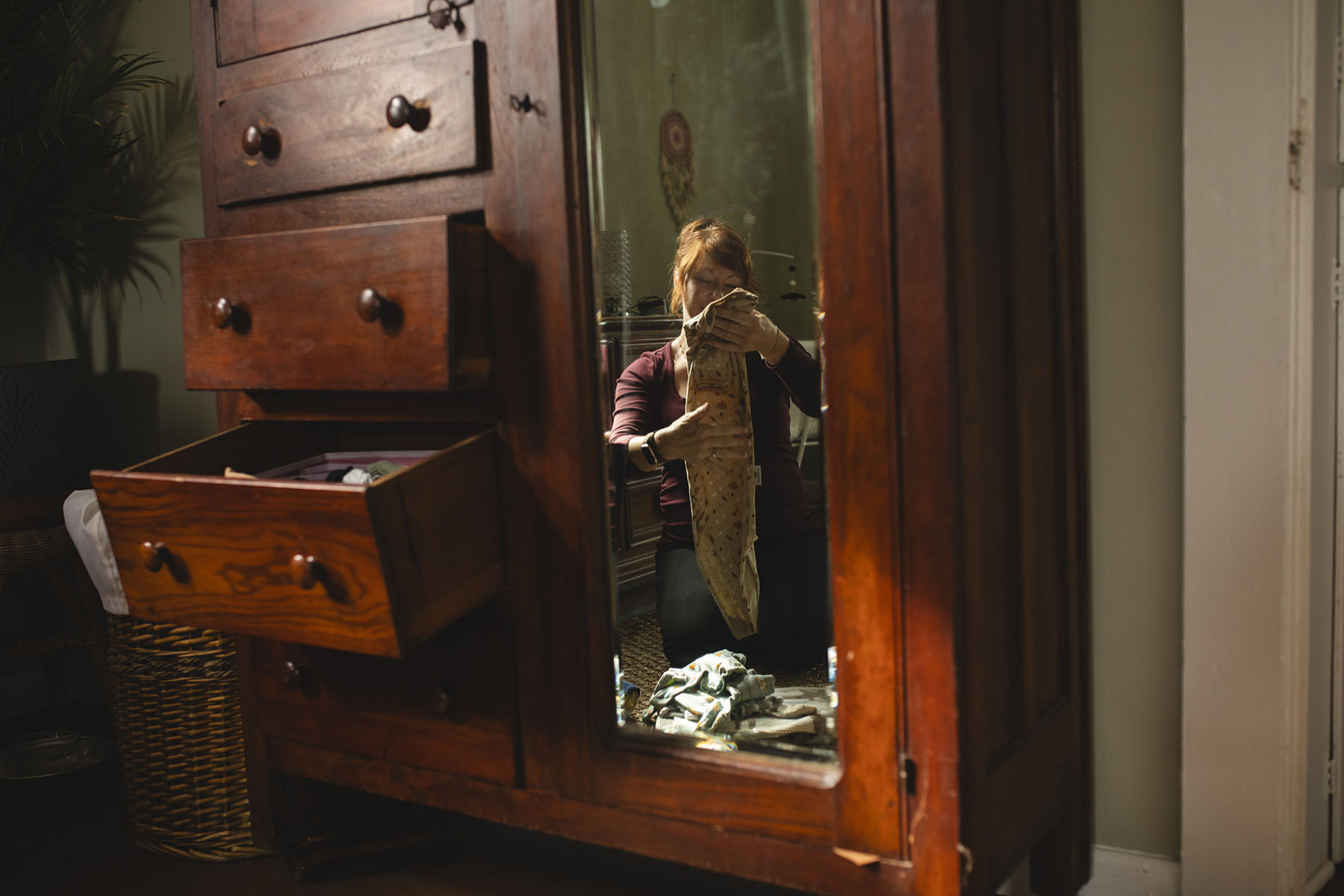 Toups is seen in a mirror as she folds baby clothes while sitting on the floor at her home.
