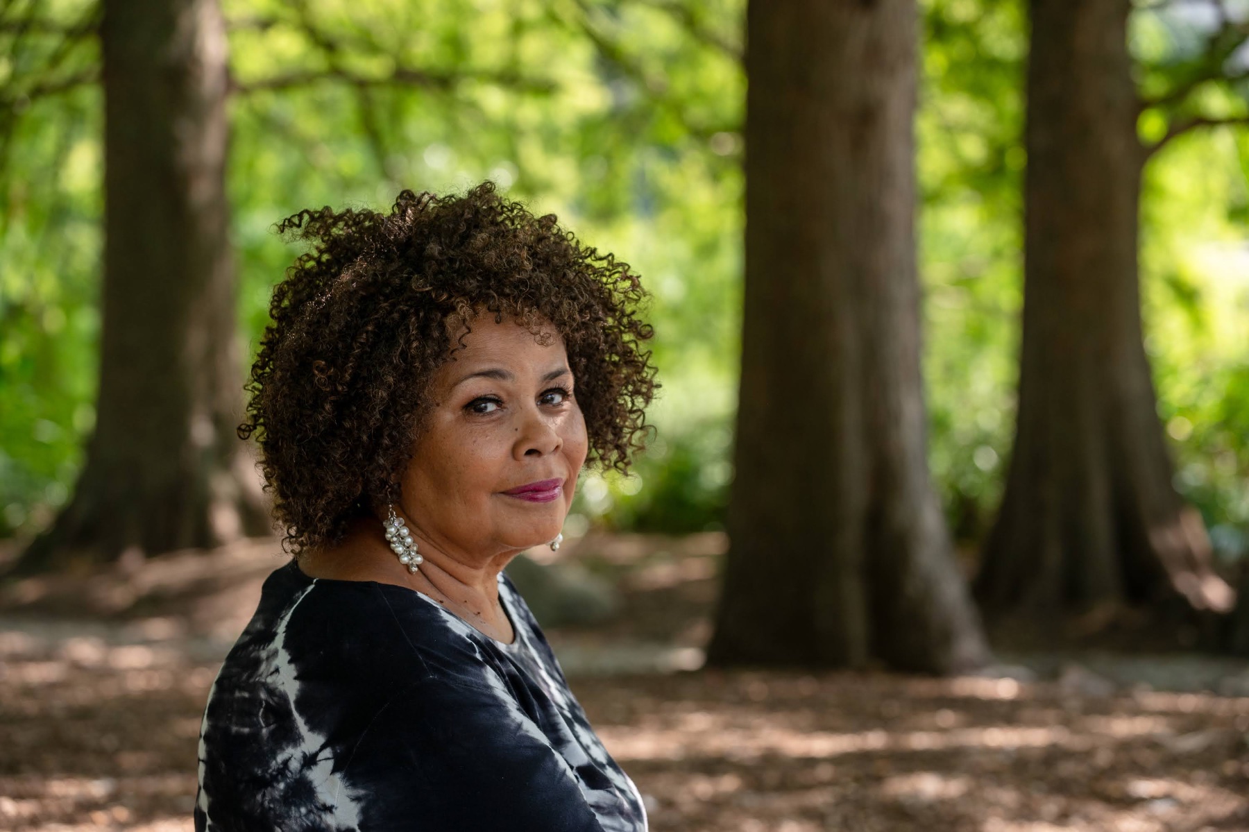 A Black woman with curly hair sits in a forest.