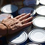 A woman's hand is seen resting on canned goods.