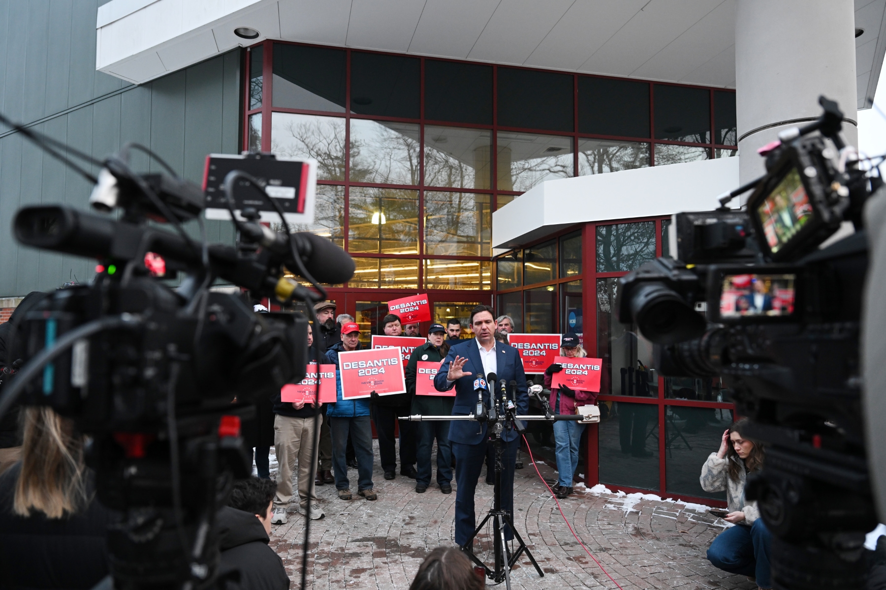 Ron DeSantis stands outside a building surrounded by camers