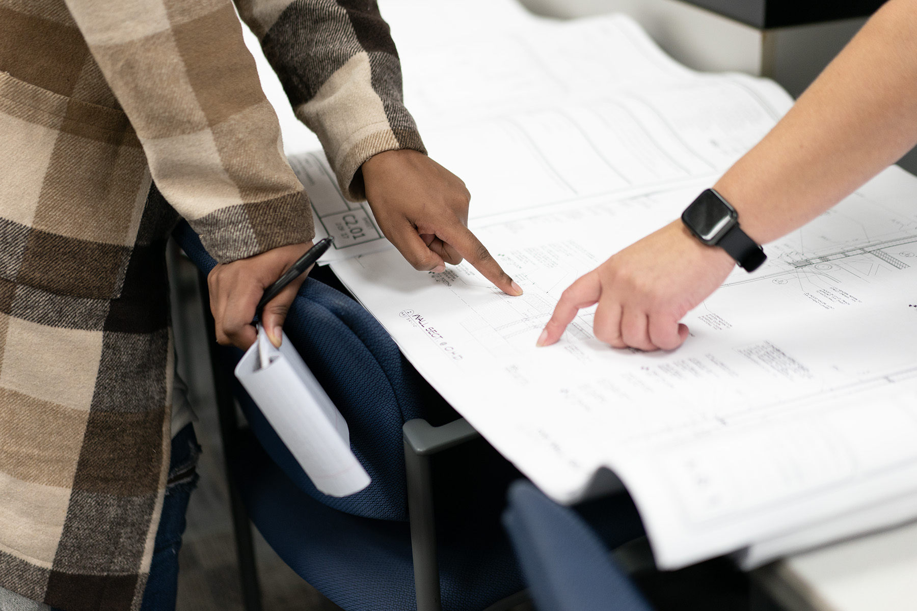 Close up shot of two people pointing to different parts of a blue print.