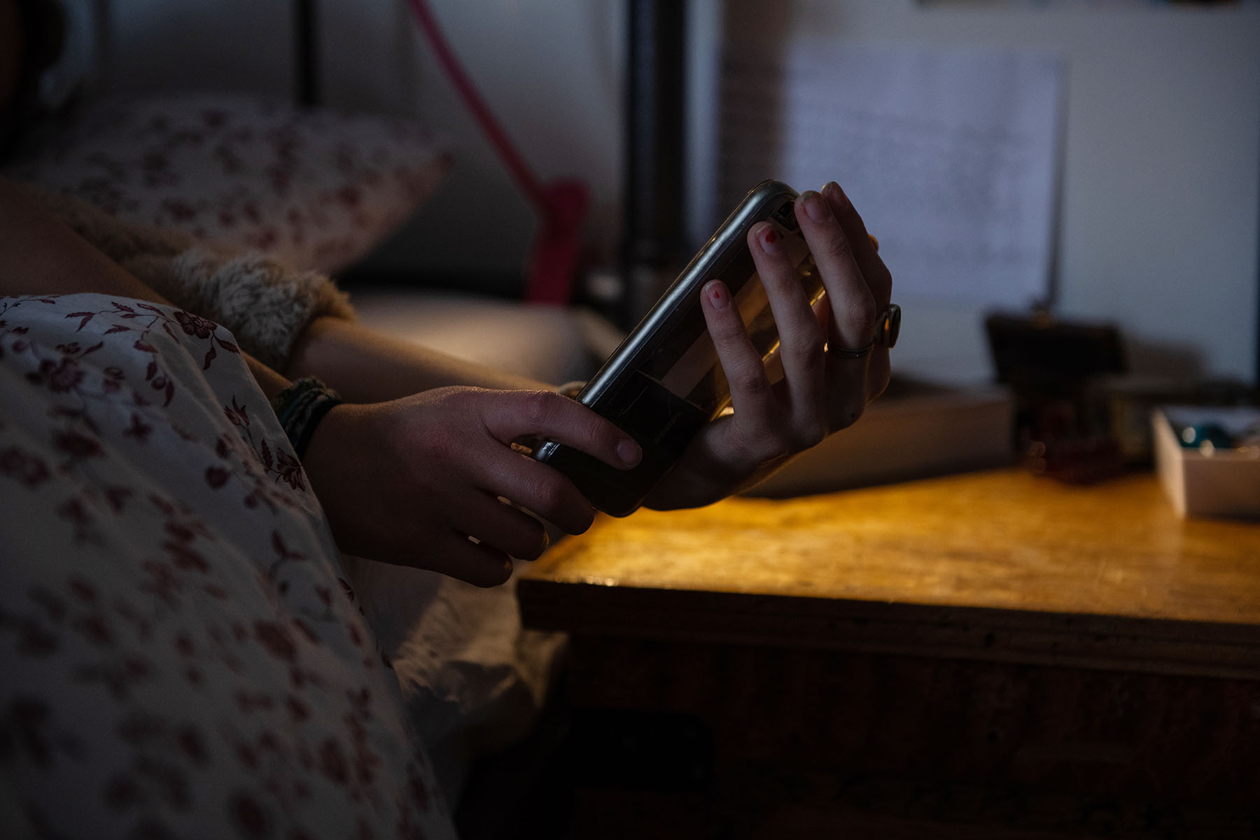 A teenager reaches for their phone at their bedside.