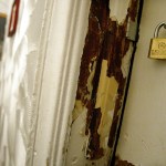 A child stands in the background near a wall of peeling paint. A doorway of peeling paint is in the foreground.