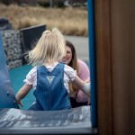 A small child is seen from the back as she plays with her mother at a playground.