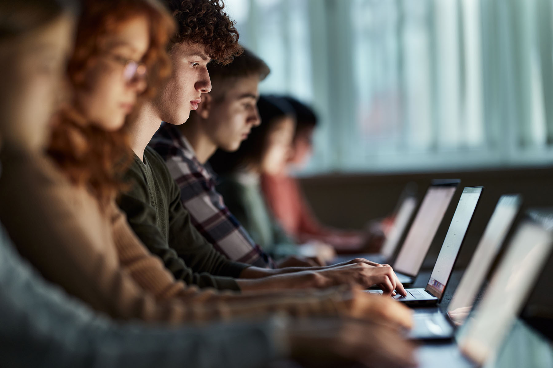 A group of high school students studying over laptops in a classroom.