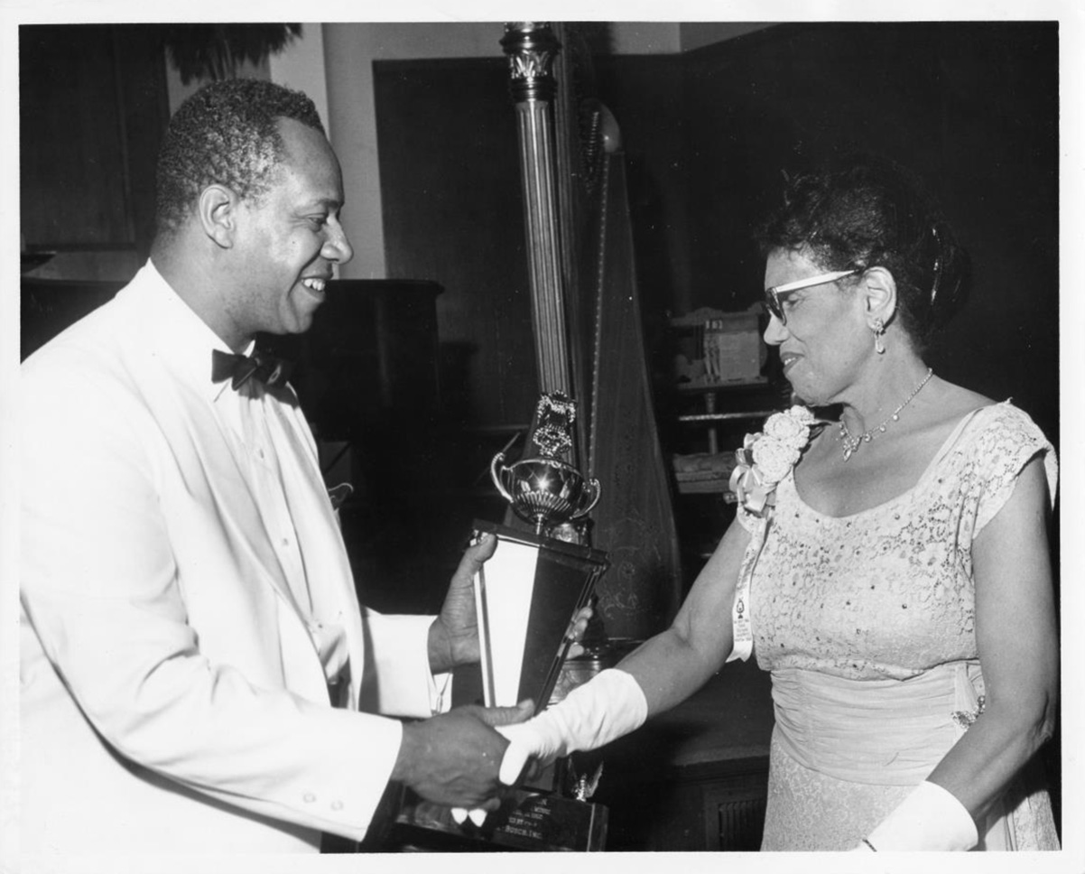 Camille Nickerson shakes hands with Kenneth Brown Billups as she receives an award.