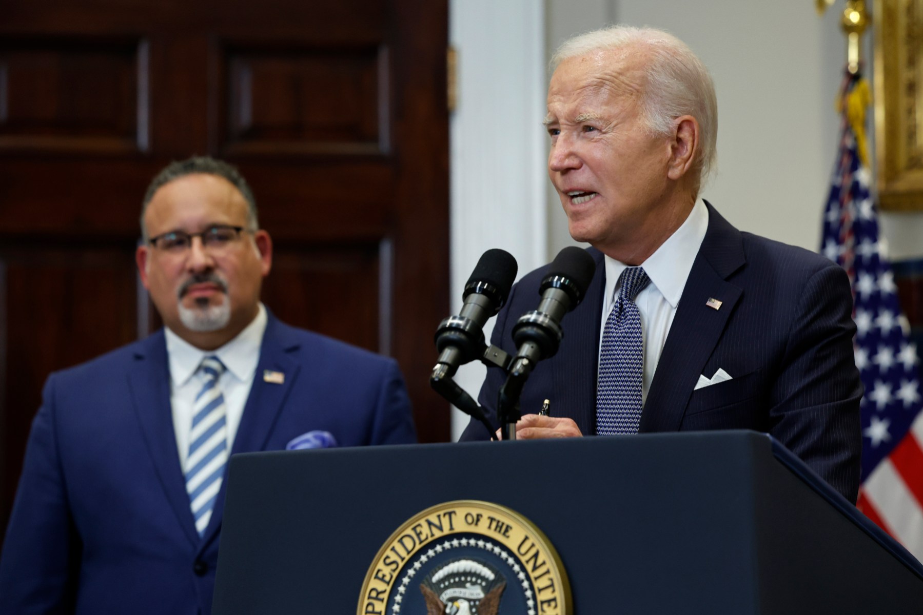 President Joe Biden is joined by Education Secretary Miguel Cardona at the White House lectern.