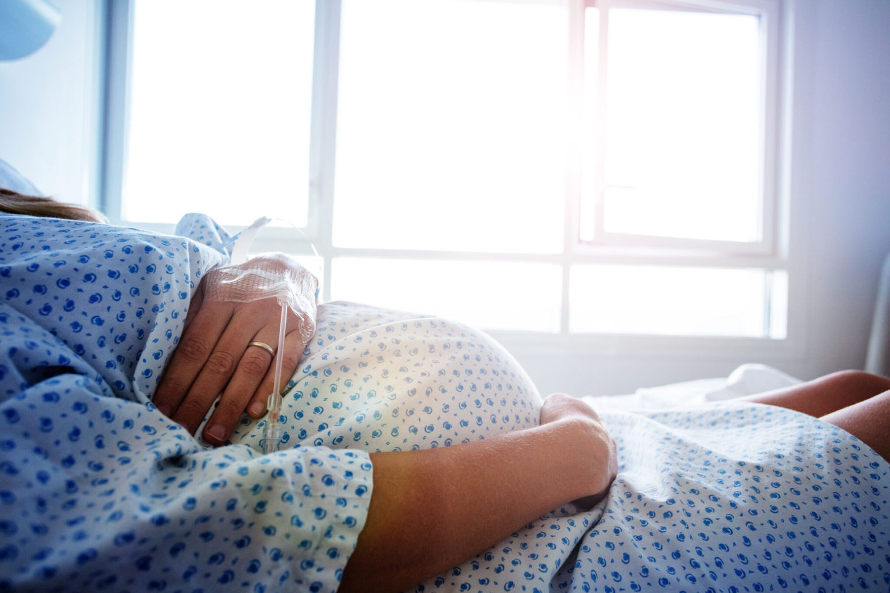 Close-up of a pregnant woman's belly in a hospital bed with a catheter in hand.