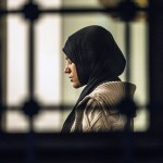 A woman is seen praying through a window at a mosque.