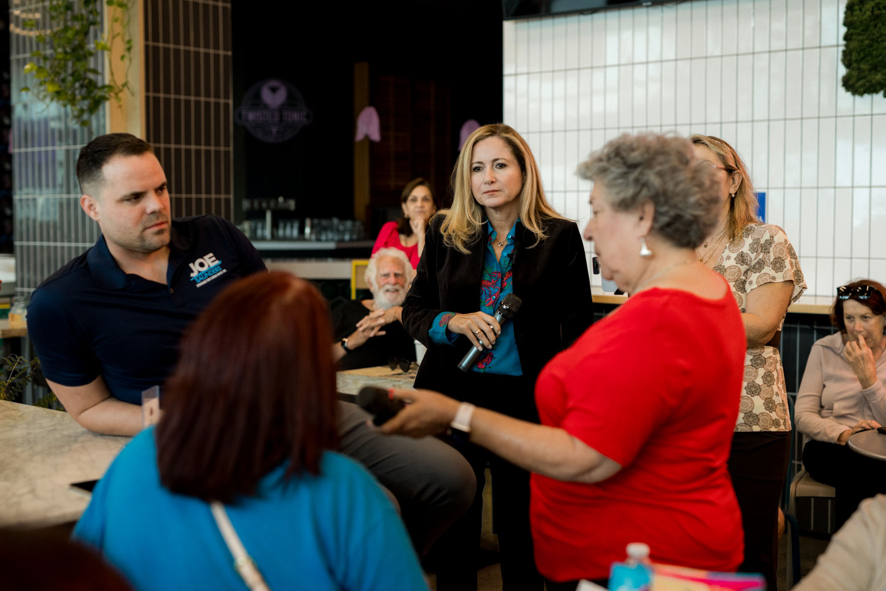 Debbie-Mucarsel-Powell listens as people ask questions into a microphone at a coffee shop during a meet and greet.