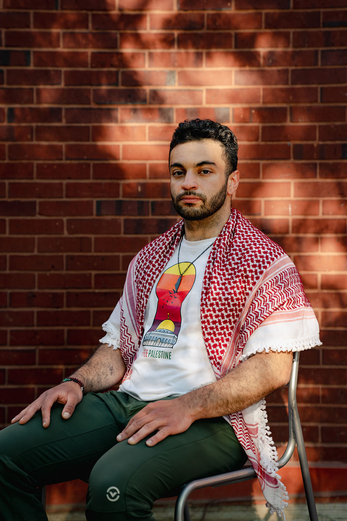 Moataz Salim sits on a chair in front of a brick wall at University Yard on the George Washington University campus.