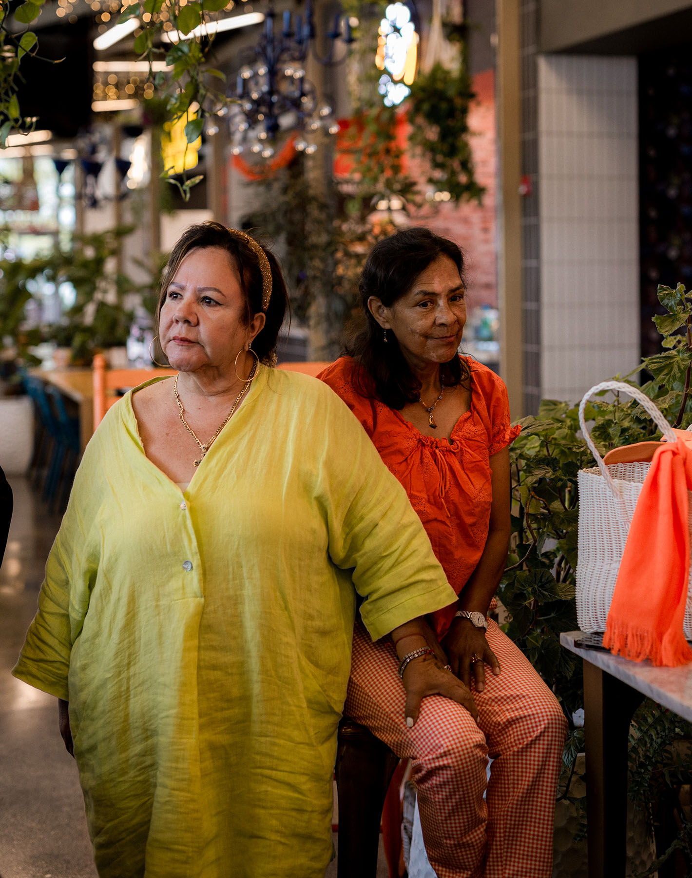 Two women, one sitting and one standing, smile as they look in opposite directions.