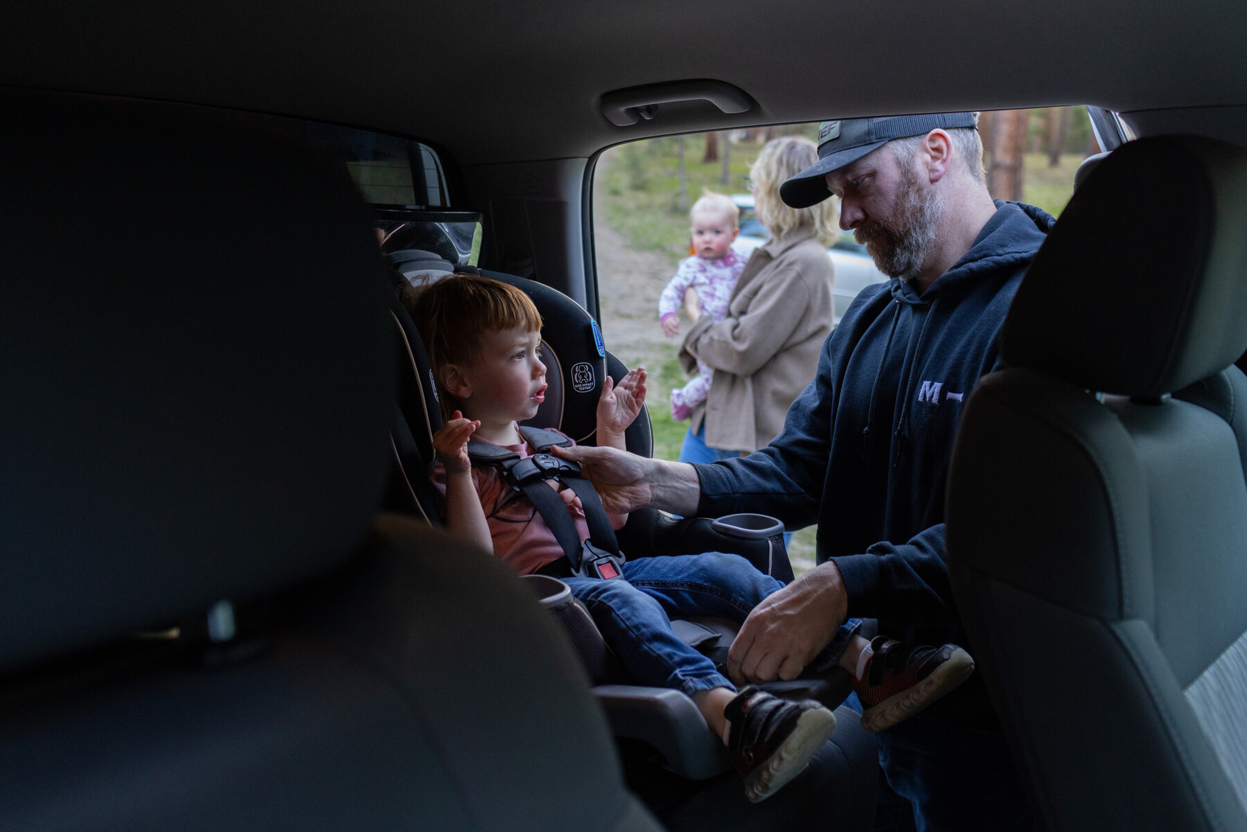 A man helps his wife buckle their 3-year-old son into a car seat.