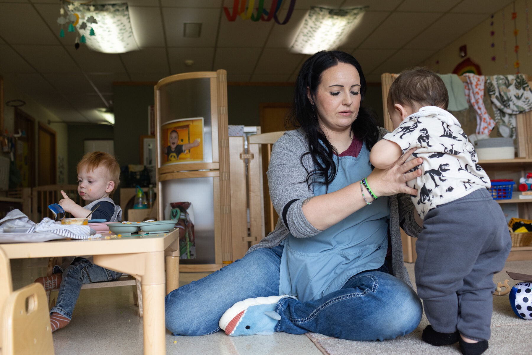 A student teacher helps an infant stand in her classroom.