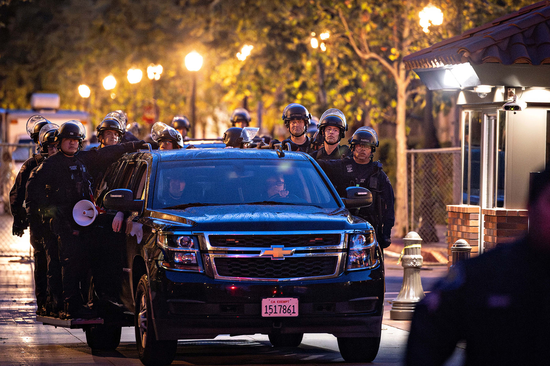 LAPD officers in riot gear ride on the side of a car as they exit USC after they cleared out a pro-Palestinian encampment.