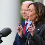 Vice President Kamala Harris speaks in front of a microphone with President Joe Biden in the background