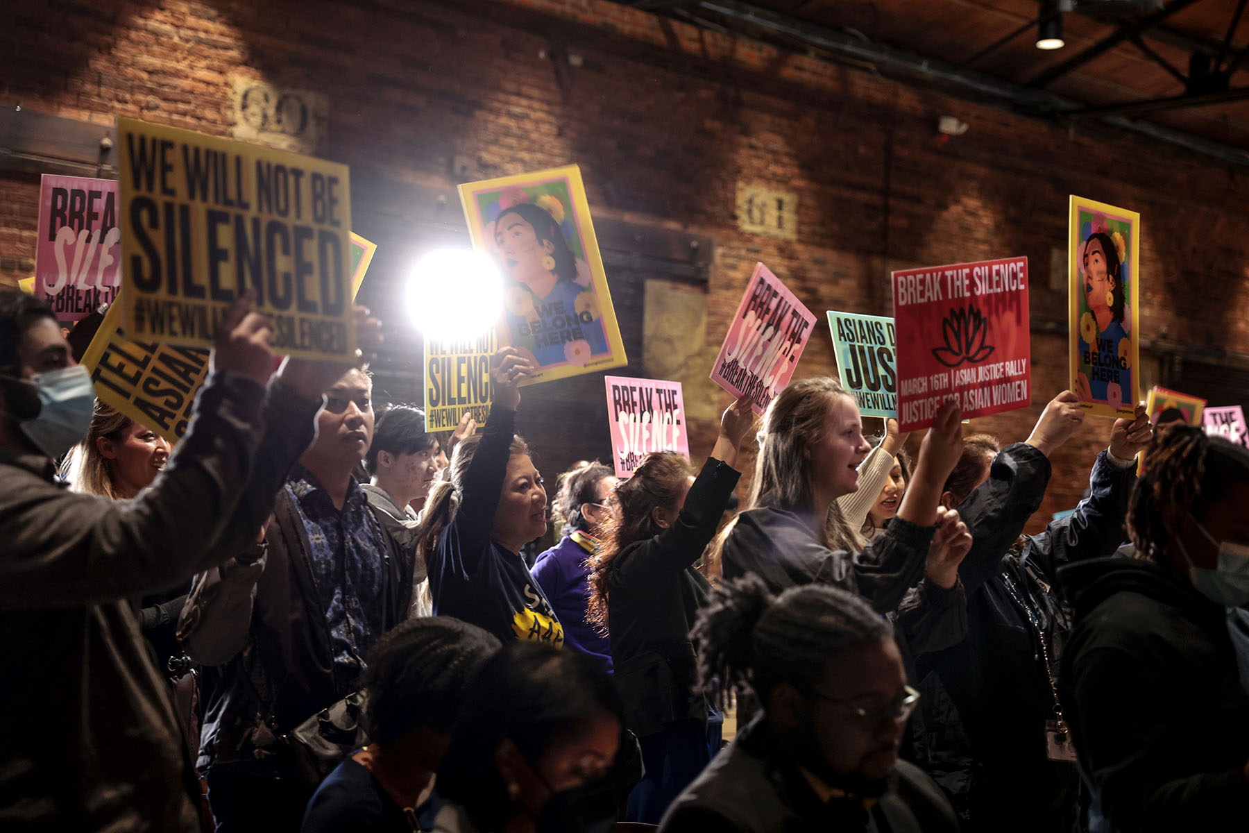 Attendees at "The Asian Justice Rally - Break the Silence" event hold up signs that read "we will not be silenced," "break the silence," and "justice for asian women"