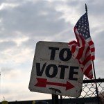 A vote sign and American flag are displayed outside a school.